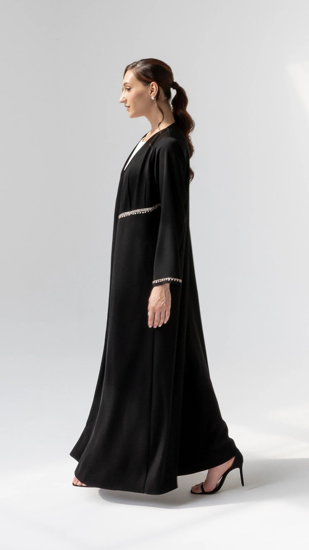 DOUNIA Noir Lumiere Side-profile luxury black abaya with flowing drape and subtle nude-gold trim accents